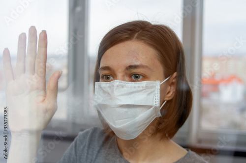 young woman in protective mask behind the glass door