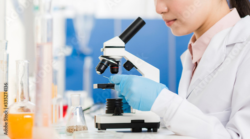 Side view of female scientist with surgical gloves looking through microscope