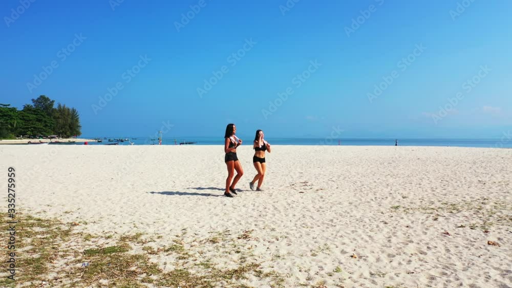 Two athlete girls warming up on tranquil white sandy beach with blue sea and bright sky background on tropical island in Thailand Two athlete girls warming up on tranquil white sandy beach with blue sea and bright sky background on tropical island in Thailand