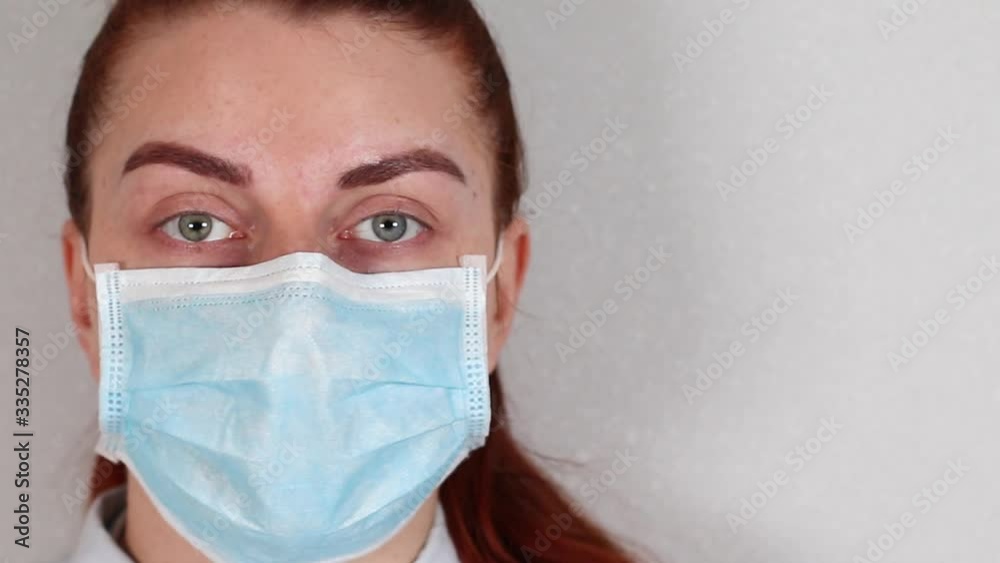 Young woman doctor face in medical mask and green eyes looks at camera with copyspace. Coronavirus, covid 19 Young woman doctor face in medical mask and green eyes looks at camera with copyspace. Coronavirus, covid 19