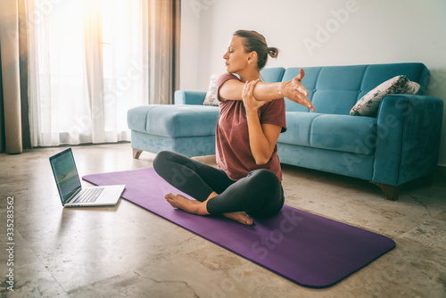 Fototapeta Attractive young woman doing yoga stretching yoga online at home. Self-isolation is beneficial, entertainment and education on the Internet. Healthy lifestyle concept