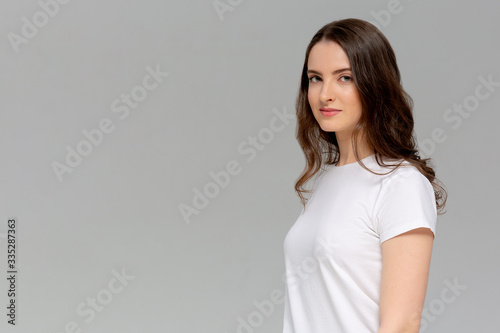 Close up portrait of serious young woman in white t-shirt looking at camera, isolated on gray background