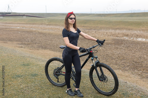 Girl on a mountain bike on offroad, beautiful portrait of a cyclist in rainy weather, Fitness girl rides a modern carbon fiber mountain bike in sportswear. Close-up portrait of a girl in red bandana.