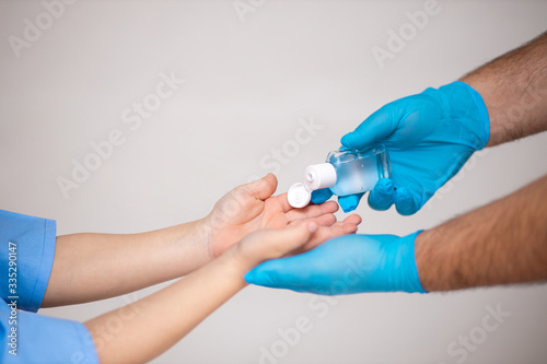 Adult male hands in medical gloves pour an antiseptic on children's hands.