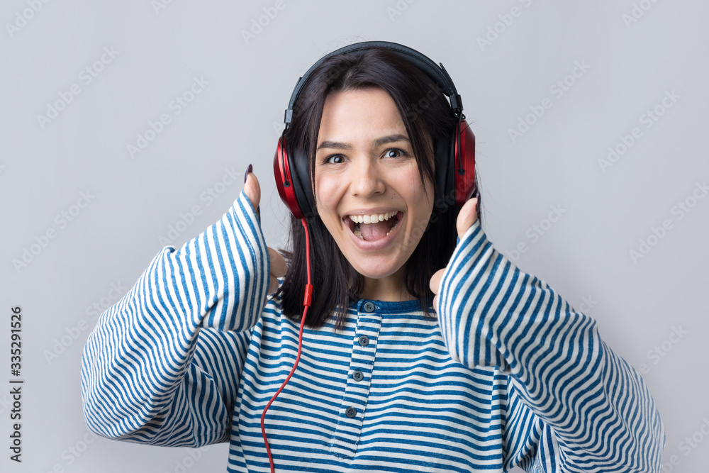 A young girl in a striped vest is listening to music in red headphones in a studio and dancing. A young girl in a striped vest is listening to music in red headphones in a studio and dancing.