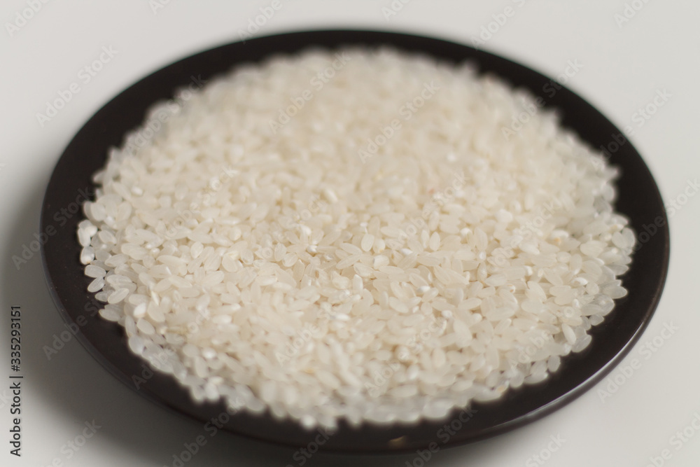 close-up of raw rice grits on a black plate on a light background. vegetarian food. close-up of raw rice grits on a black plate on a light background. vegetarian food.