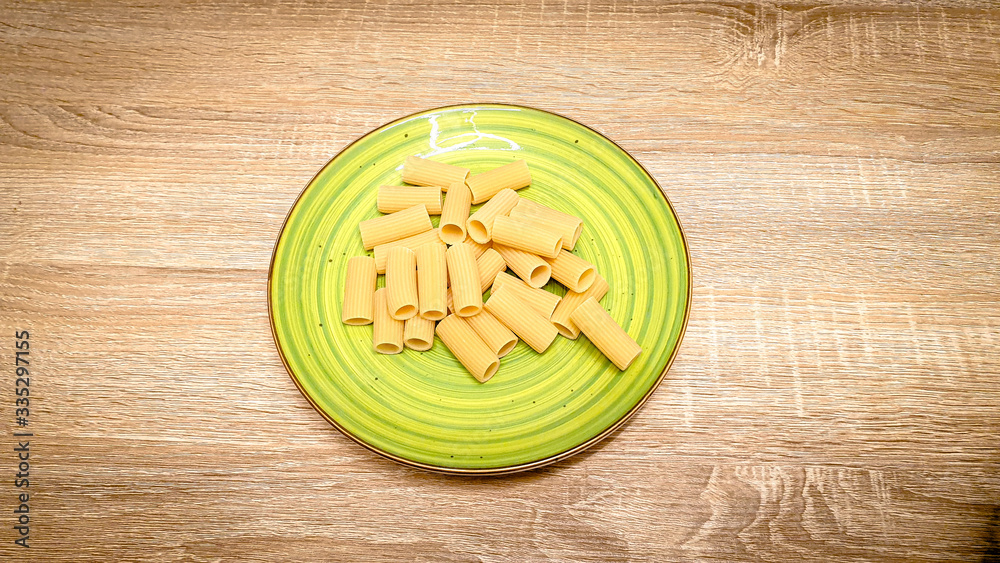 Uncooked raw rigatoni pasta on a green plate on wood background. Top view, selectiv focus, with copy space, space for text. Uncooked raw rigatoni pasta on a green plate on wood background. Top view, selectiv focus, with copy space, space for text.