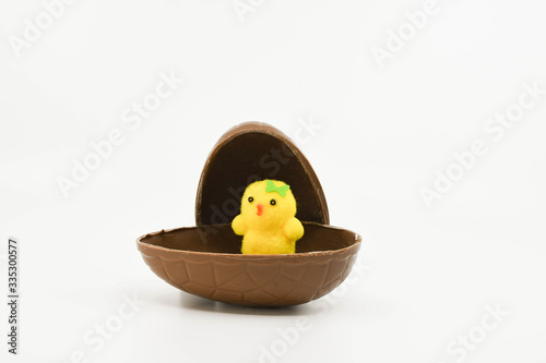 Single small yellow model chick sitting in half a chocolate Easter egg isolated on a plain white background