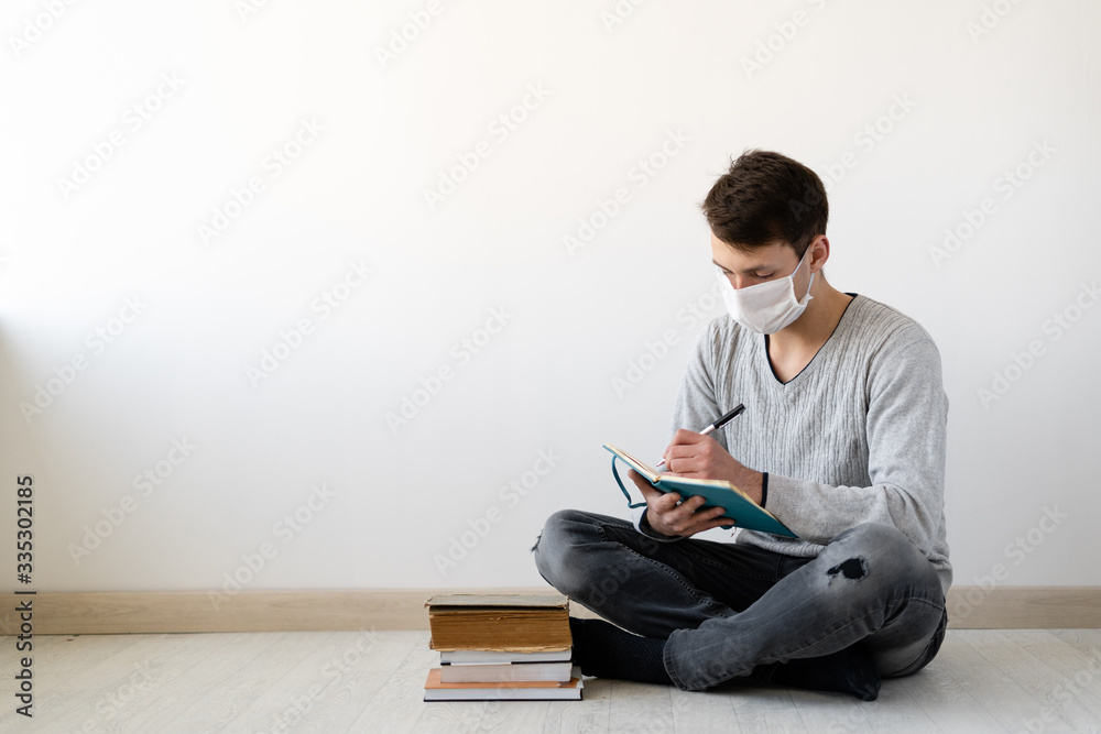 training during a pandemic and coronavirus. A young guy sits at home on the floor is engaged in education. Reading books and learning on deleted.