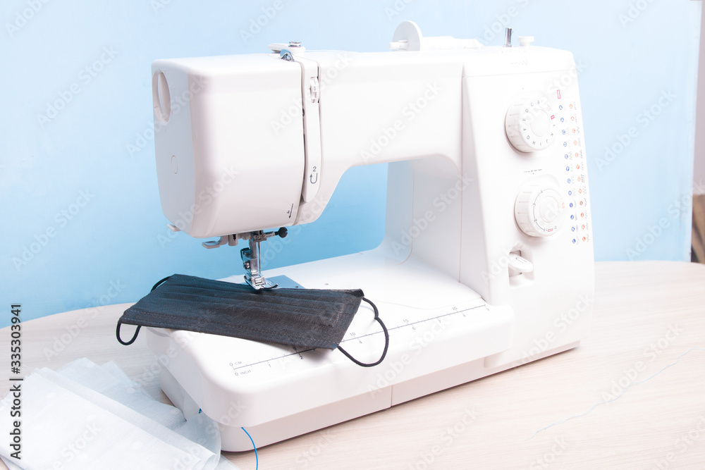 disposable black face shield and homemade multi-face mask lie on the sewing machine, blue background, make yourself a protective mask from the fabric at home, do-it-yourself protective mask