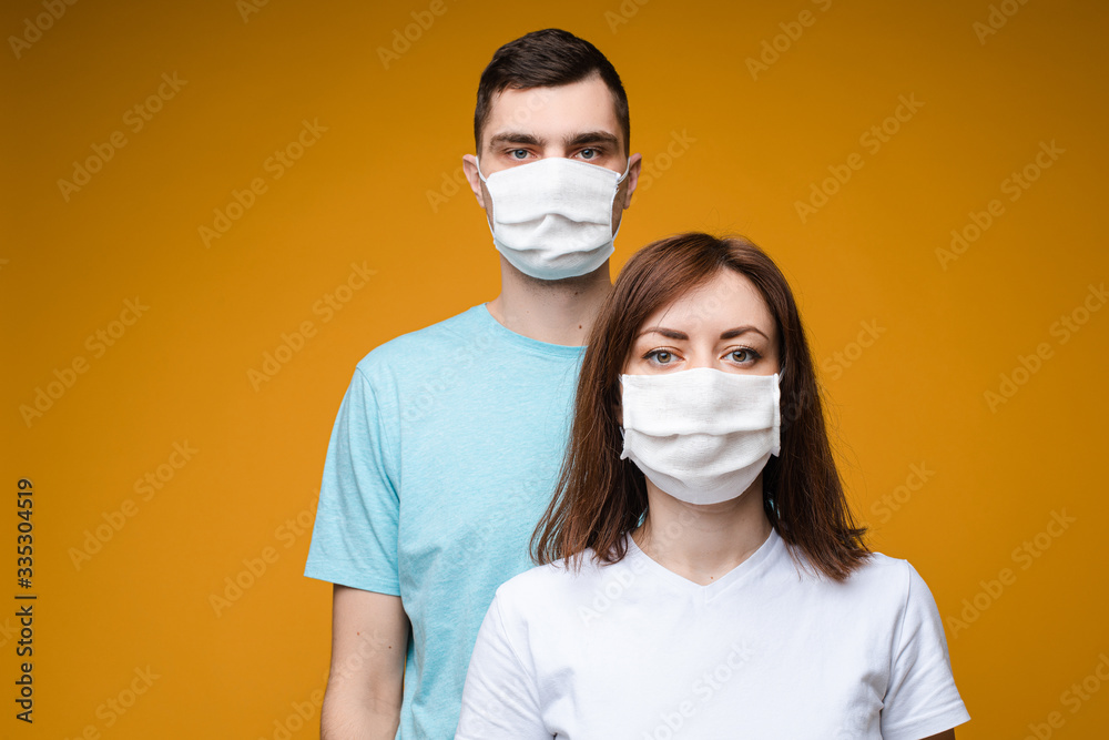 Studio portrait of two young people wearing handmade antibacterial disinfectant masks. Isolate on yellow background.