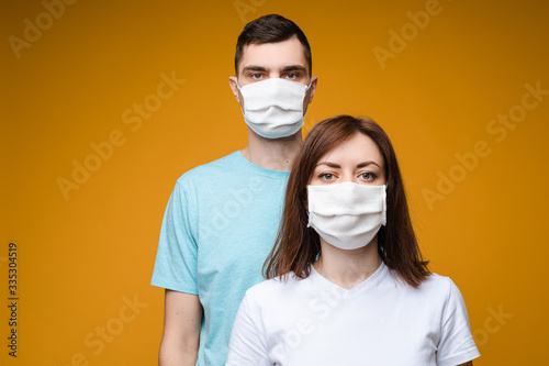 Studio portrait of two young people wearing handmade antibacterial disinfectant masks. Isolate on yellow background. © Вячеслав Косько