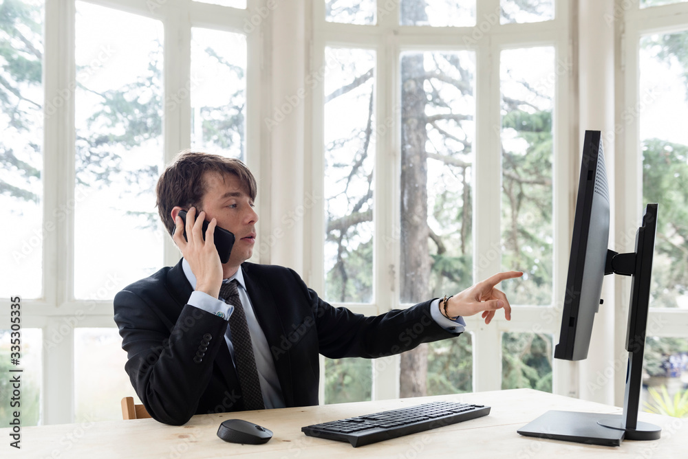 Caucasian man on a suit working on a desk and talking on the phone