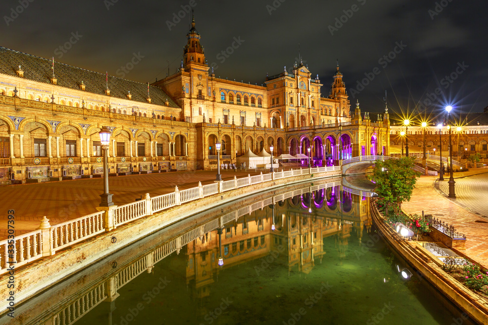 Renaissance building in Plaza de Espana in Seville, Andalusia, Spain, reflects on channel of Guadalquivir river. Scenic Spain Square illuminated at night, popular landmark.