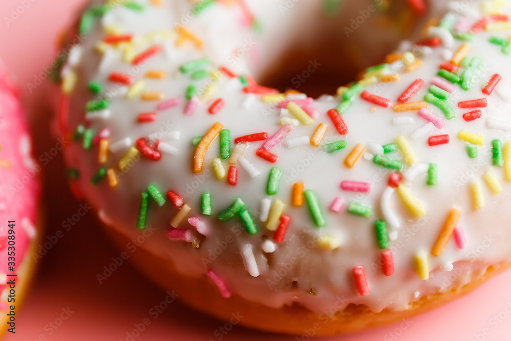 Two juicy fresh sweet donuts with sugar icing and sprinkles on a pink background
Two juicy fresh sweet donuts with sugar icing and sprinkles on a pink background