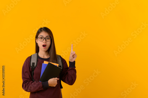 Fotografija Portrait photo of young attractive looking Asian college student with shocking or surprising face emotion pointing at copy space on yellow background