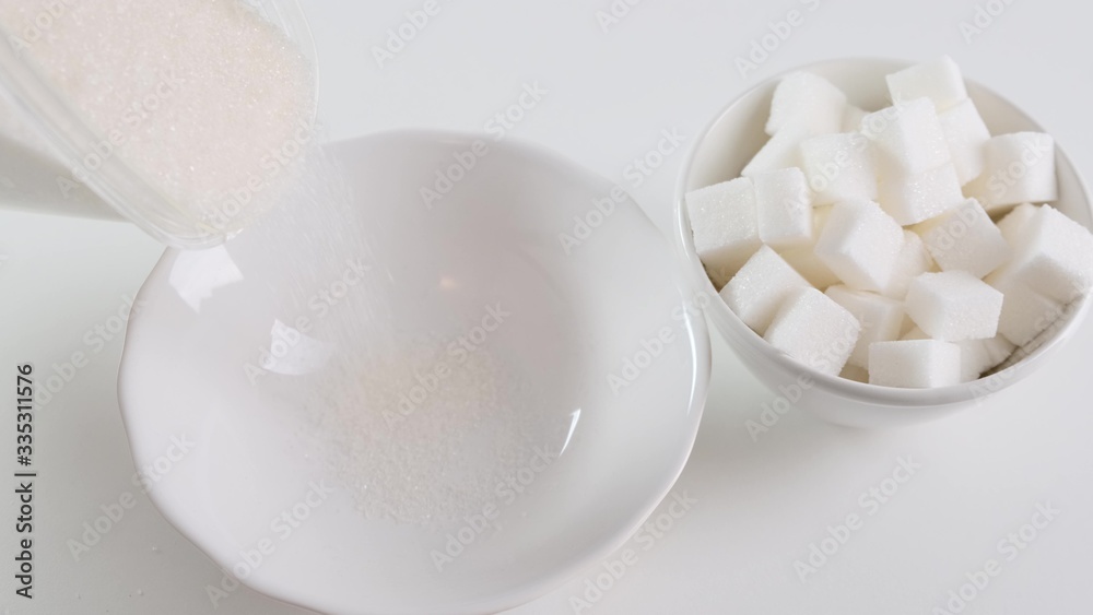 Sugar poured into a small white bowl on background. Close up. Sugar poured into a small white bowl on background. Close up.