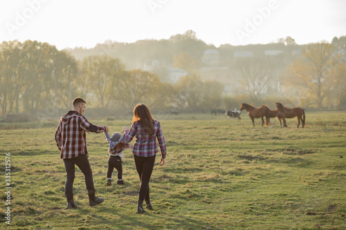 Family with cute little son. Father in a red shirt. People walking near horses.