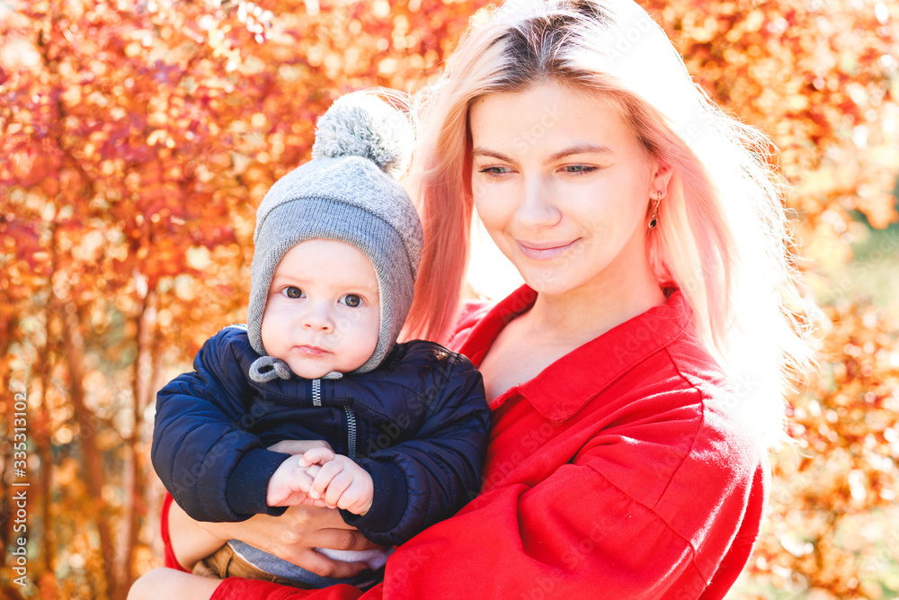 A stylish young mother with a small son in her arms walks in the autumn.