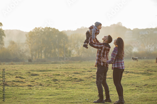 Family with cute little son. Father in a red shirt. People walking near horses. © hetmanstock2