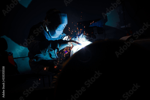 the process of welding pipes by a masked welder with flying sparks and glow