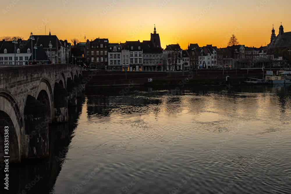 Naklejka premium Sunset in early April with a view on the river Meuse, the old roman Sint Servaas bridge and the skyline of Maastricht