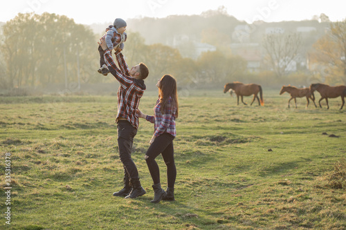 Family with cute little son. Father in a red shirt. People walking near horses.