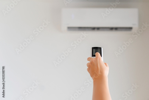 Brunette woman holding remote controller from air conditioner inside the room. Back view.