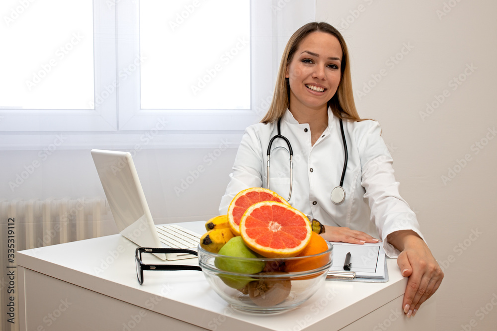 Female nutritionist with fruits working at her desk. Smiling nutritionist in her office, she is showing healthy vegetables and fruits, healthcare and diet concept. 