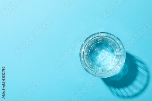 Glass of water on blue background, top view