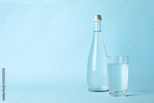 Glass and bottle with water on blue background, space for text