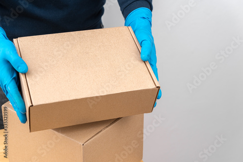 Contact less delivery concept, safe shipment, courier in a protective mask and rubber gloves with carboard box , order from online shop, copy space. © OlegKovalevich