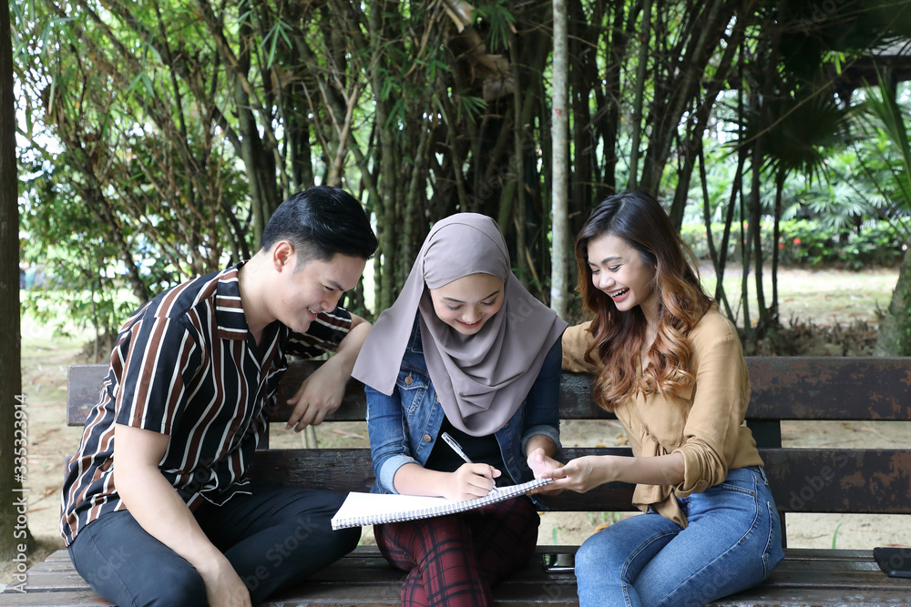 Young Asian Malay man woman headscarf outdoor green sit on park bench paint draw talk mingle Young Asian Malay man woman headscarf outdoor green sit on park bench paint draw talk mingle