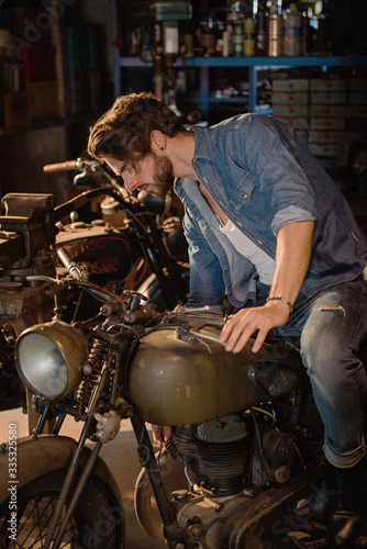A young man with a hipster look works in his workshop repairing vintage motorcycles.