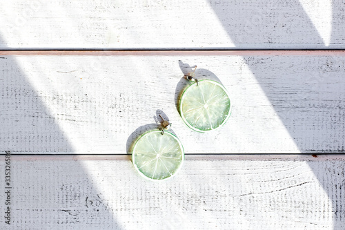 earrings in the shape of green lime slices on a white wooden background
