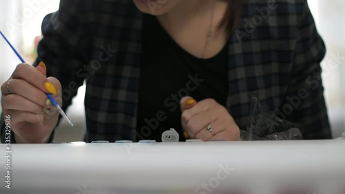 Creative young woman is painting a picture sitting at a table with a thin brush inside photo