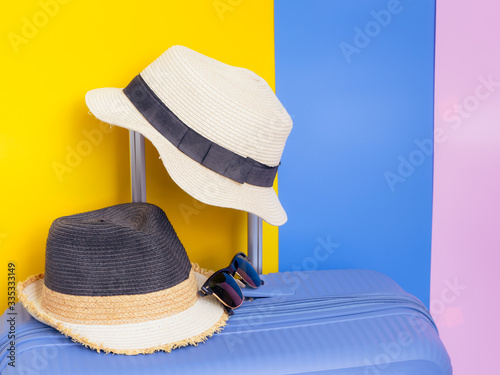 colorful in summer travel concept from modern blue luggage with two vintage summer hat with blue , pink and yellow pastel background