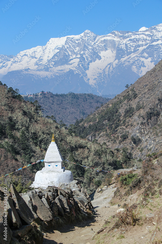 View of typical white stone tibetan buddhist stupa in Himalayas next to mani sones on footpath to Everest Base Camp. Kangtega mountain in the background.