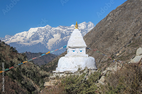 View of typical white stone tibetan buddhist stupa in Himalayas next to mani sones on footpath to Everest Base Camp. Kangtega mountain in the background.