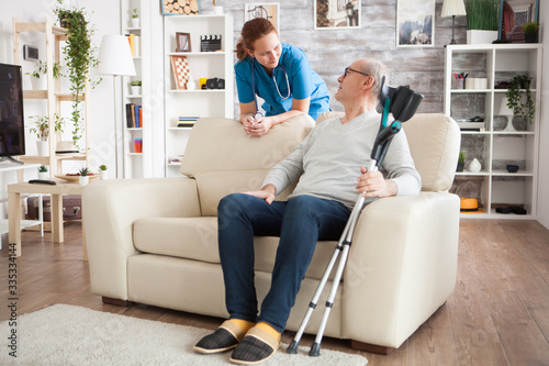 Foto Old man sitting on couch holding his crutches