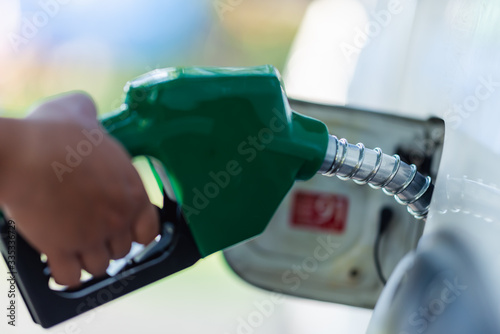 Handle pumping gasoline fuel nozzle to refuel. Vehicle fueling facility at petrol station. White car at gas station being filled with fuel. Transportation and ownership concept.