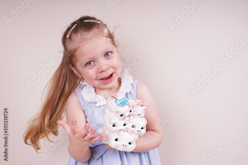 Little girl with a piggy bank. Child emotions and money theme. Photo taken on a light isolated background, straight view.