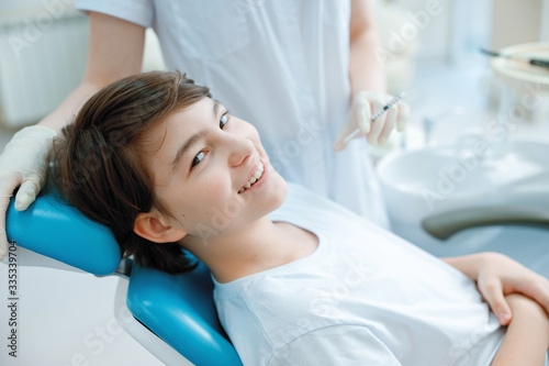 Woman doing injection to teen boy, selective focus. Female doctor with vaccine shot in hand. Healthcare concept. Nurse with syringe. Happy teenager in clinic.