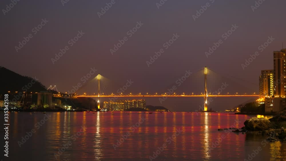 Colourful time lapse shot of brightly illuminated Ting Kau Bridge at night, car lights run along road, airlines move upwards in sky. Nice reflection at water surface Colourful time lapse shot of brightly illuminated Ting Kau Bridge at night, car lights run along road, airlines move upwards in sky. Nice reflection at water surface