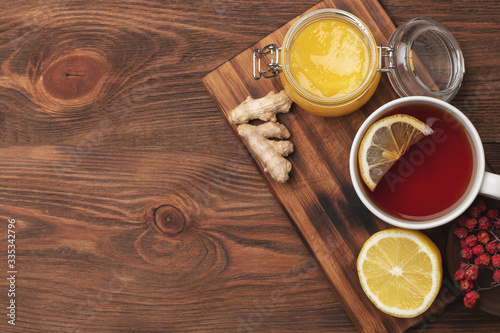 flat lay of natural ingredients for tea to increase immuntiy during self-isolation period. lemon on a wooden plate, ginger, hot tea and honey in a wooden spoon.