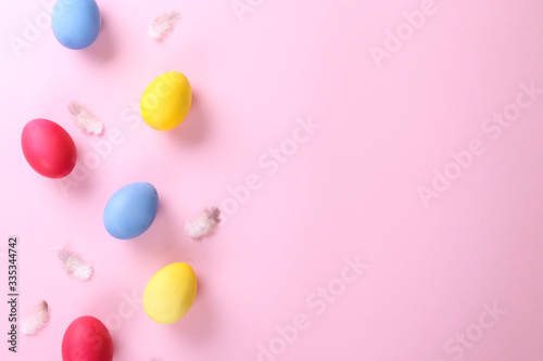 Bunch of blank painted Easter eggs of different bright colors on pink paper texured background with a lot of copy space for text. Top view, flat lay, close up.