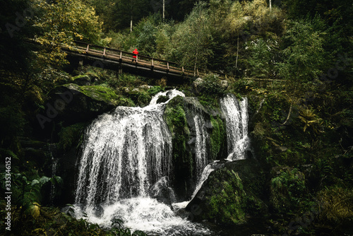 Triberger Wasserfall mit einer Brücke und Person in roter Jacke oberhalb des Wasserfalls. photo