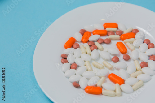 Multi-colored pills in a white plate on a blue background