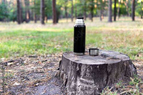 Black thermos bottle and a cup on a stump in a park in early fall