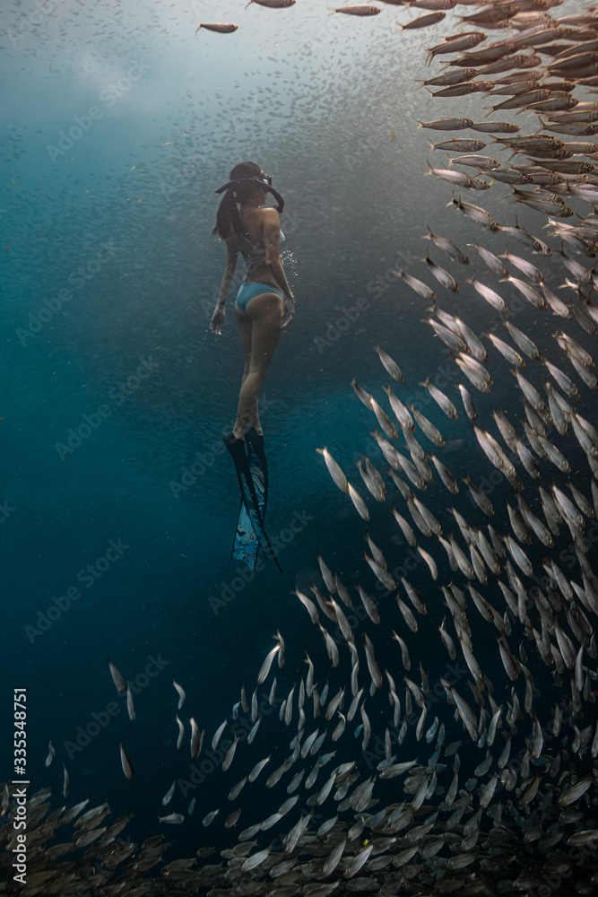 Young female free diver in a sexy swimwear ascends to the surface coming from a deep dive.